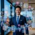 都市を背景に立つスーツ姿の経営者と、SNS・新聞・メディアを象徴するアイコンを組み合わせ、社会的評価とパーソナルブランディングを表現した画像